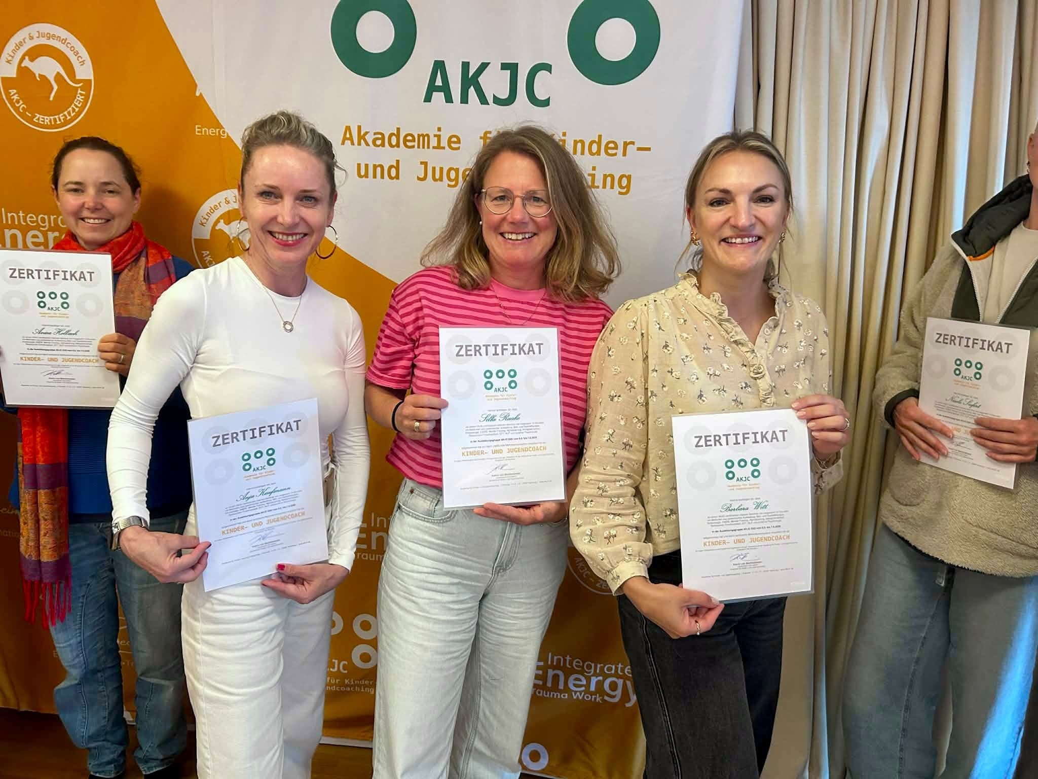 Absolventinnen halten ihre Zertifikate «Kinder- und Jugendcoach» vor dem AKJC-Banner